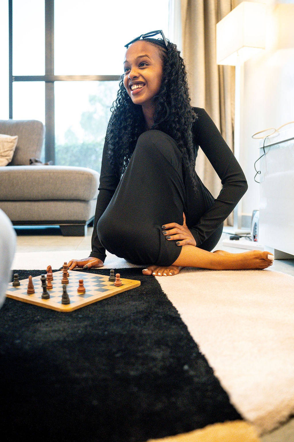 Smiling woman sitting on Mosiac artisan rug playing chess